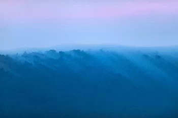 Blauw gekleurde wolken spreiden zich over heuvel met blauw tot roze gekleurde lucht